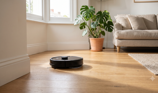 Modern UK living room with hardwood floor, a compact robot vacuum and mop in motion beside a tidy sofa and potted plant