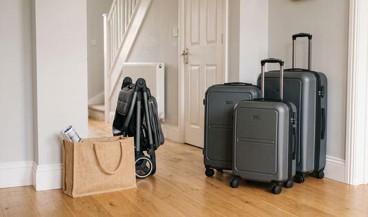 Compact lightweight ABS hard-shell trolley suitcases in navy and grey arranged beside a folded pram and reusable shopping bag