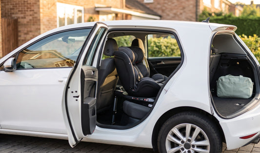 A modern UK family loading a Reecle 360 swivel ISOFIX car seat into a compact hatchback in a sunlit driveway