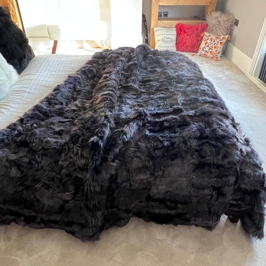 Black fur throw blanket on a bed with pillows in the background